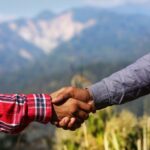 Two people shaking hands outdoors with blurred mountains and greenery in the background signifying client retention