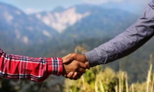 Two people shaking hands outdoors with blurred mountains and greenery in the background signifying client retention