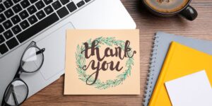 Thank-you card with a leafy design placed on a laptop, next to glasses, a notebook, and a cup of coffee