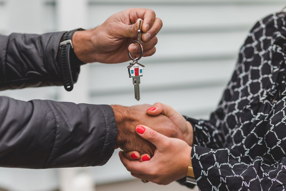 A real estate agent and a happy client shaking hands in front of a beautiful modern home, symbolizing a successful and profitable sale.