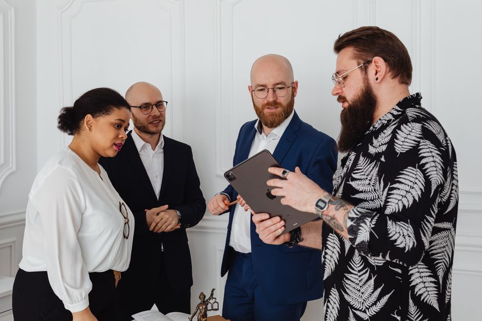 A diverse group of professionals in a bright, modern office collaborating around a table with a tablet, discussing a digital marketing strategy for a real estate project.