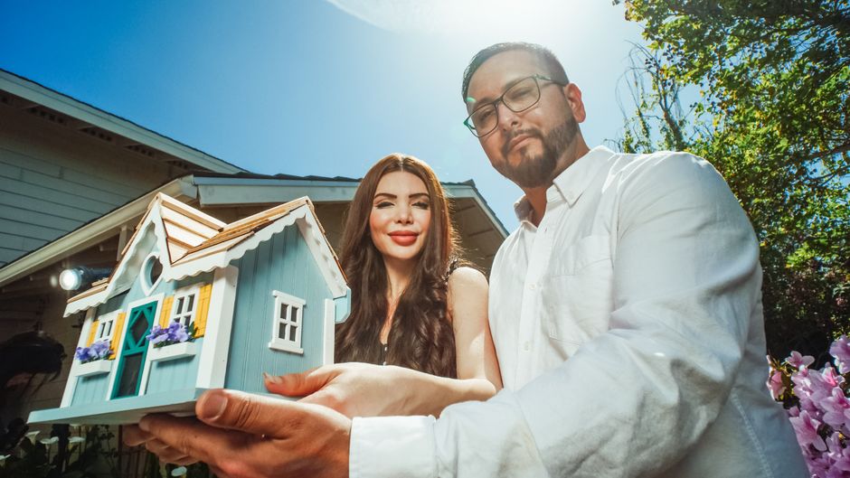 A pair of hands gently holding and protecting a miniature white model of a house against a clean background, representing home investment protection.